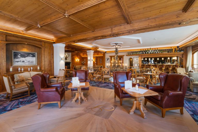 Ledersessel gruppiert um Tische in einer gemütlichen, holzgetäfelten Hotel-Lobby mit Kronleuchter und Bar.