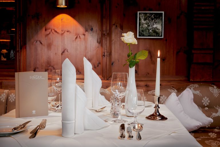 Gedeckter Tisch mit Menü "SINGER", gefalteten Servietten, Weingläsern und brennender Kerze in holzgetäfeltem Restaurant.