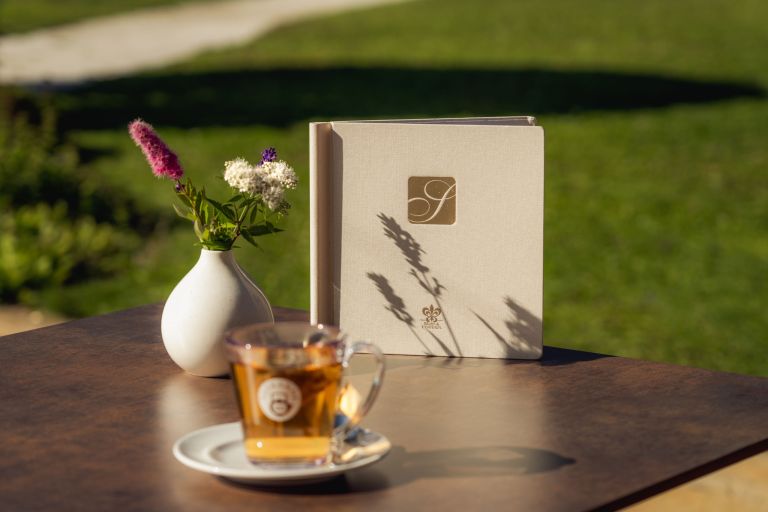 Blumenvase mit Blumen steht neben einem Menü auf einem Holztisch im Garten - davor eine volle Teetasse.