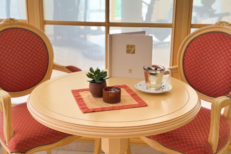 Zwei rote Sessel und ein runder Tisch mit Tasse, Sukkulente und Menü vor einer Fensterfront.