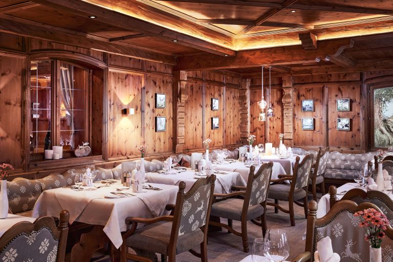 Gedeckte Esstische mit Tischtüchern und Weingläsern, arrangiert in einem warm beleuchteten, holzgetäfelten Restaurant.