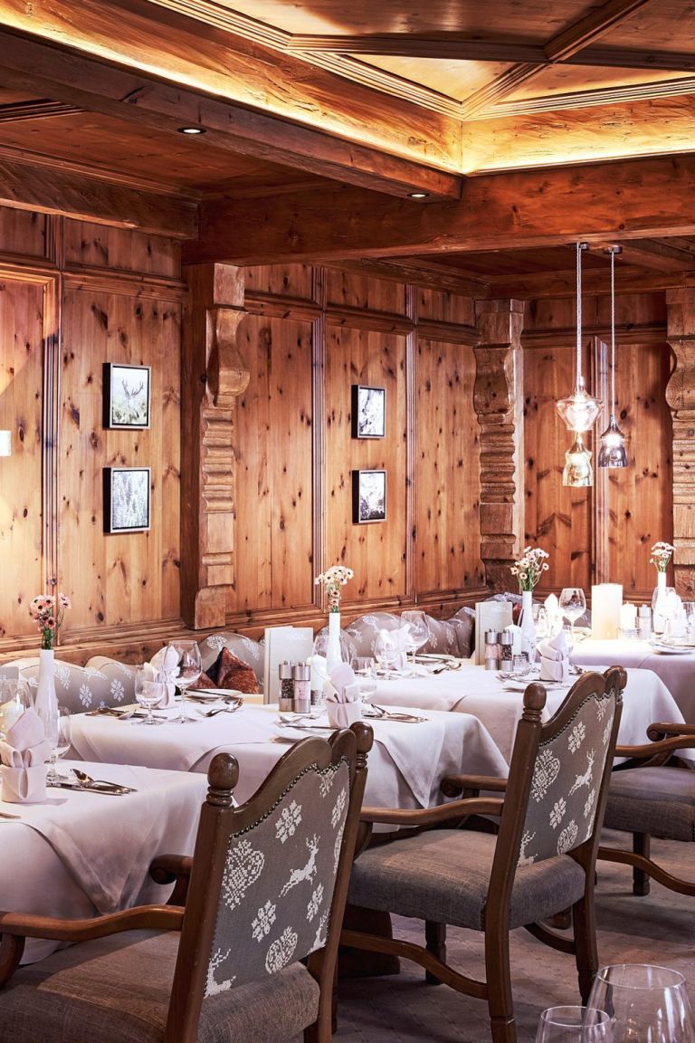 Gedeckte Tische in einem gemütlichen, holzvertäfelten Restaurant mit bestickten Stühlen, frischen Blumen und warmen Hängelampen.