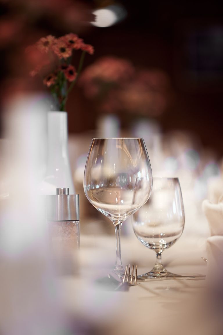Een detailfoto van een gedekte tafel met wijnglazen en bloemen in de Zirbenstube van Hotel Singer.
