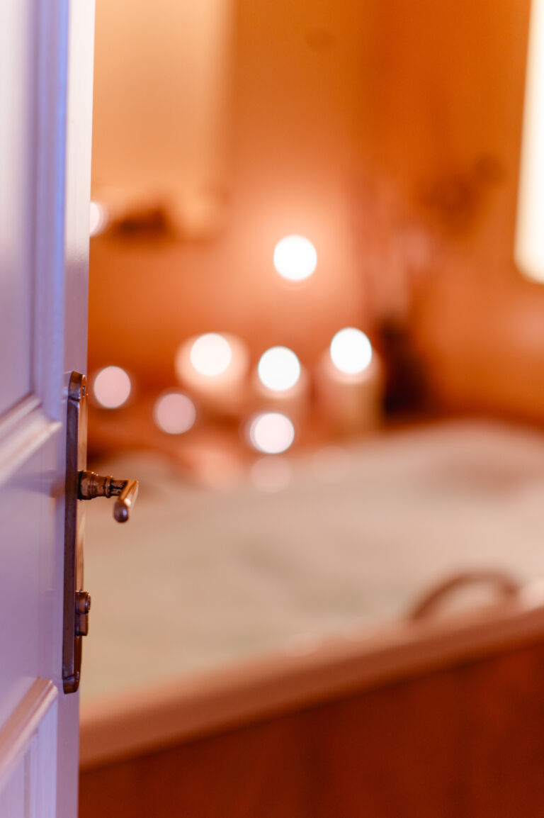 Een open deur leidt naar een badkamer bij kaarslicht; op de achtergrond staat een badkuip in Hotel Singer in Berwang.