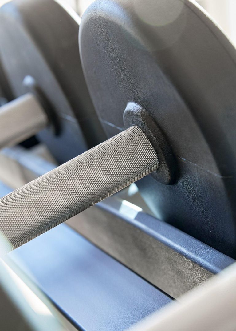 Kurzhantel mit genarbtem Griff in einem Hantelständer, umgeben von schwarzen Gewichtsscheiben im Fitnessraum.
