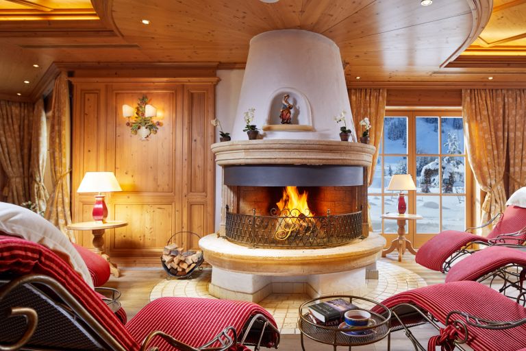Kamin brennt hell; umgeben von roten Liegesesseln und Holzvertäfelung in gemütlichem Zimmer mit verschneiter Aussicht.