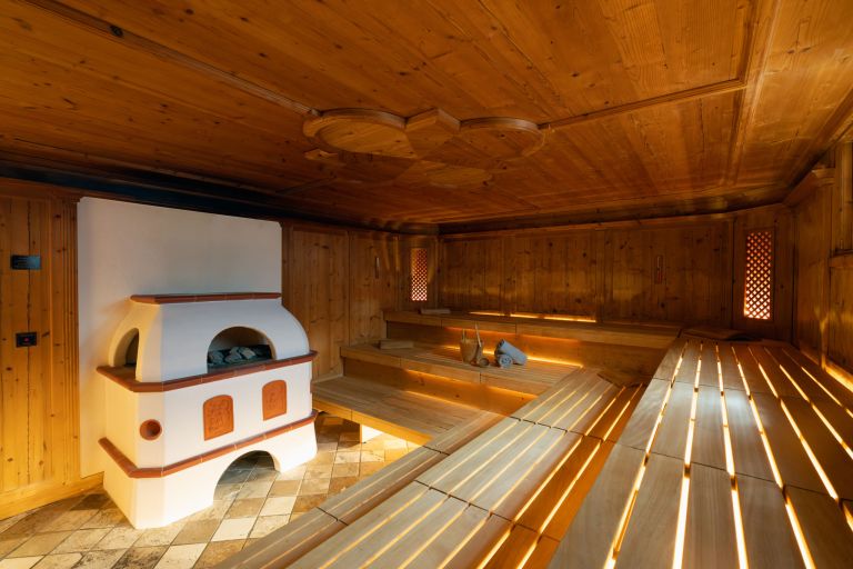 Holzbänke bieten gestaffelte Sitzplätze in einer holzvertäfelten Sauna mit Aufgussofen, Kelle und Handtüchern.