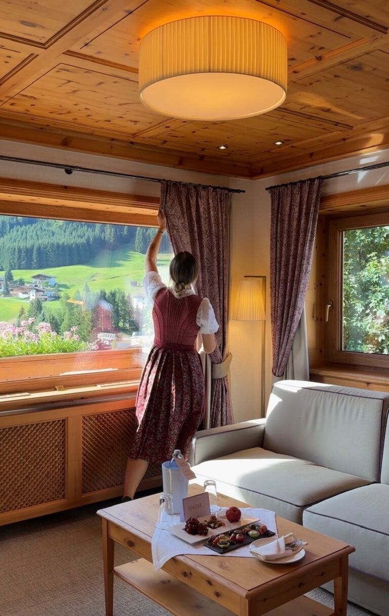 Eine Dame die die Vorhänge richtet für die Ankunft in der Hönig Suite des Hotel Singers.